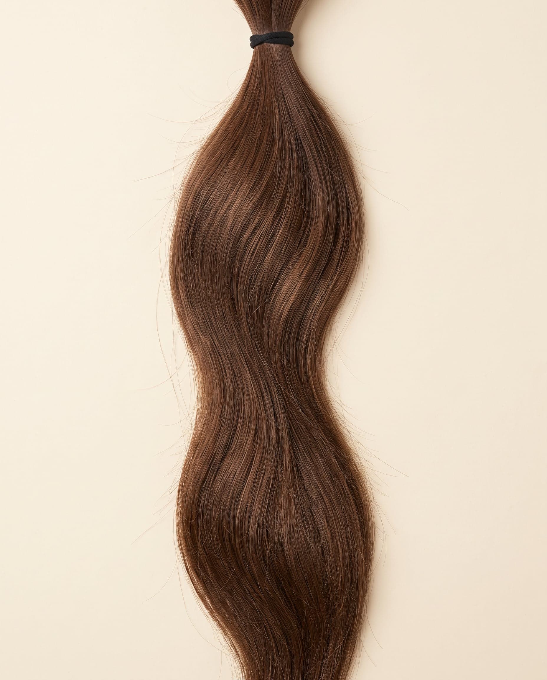 Human hair bundle in color 4 laid flat on a warm ivory background