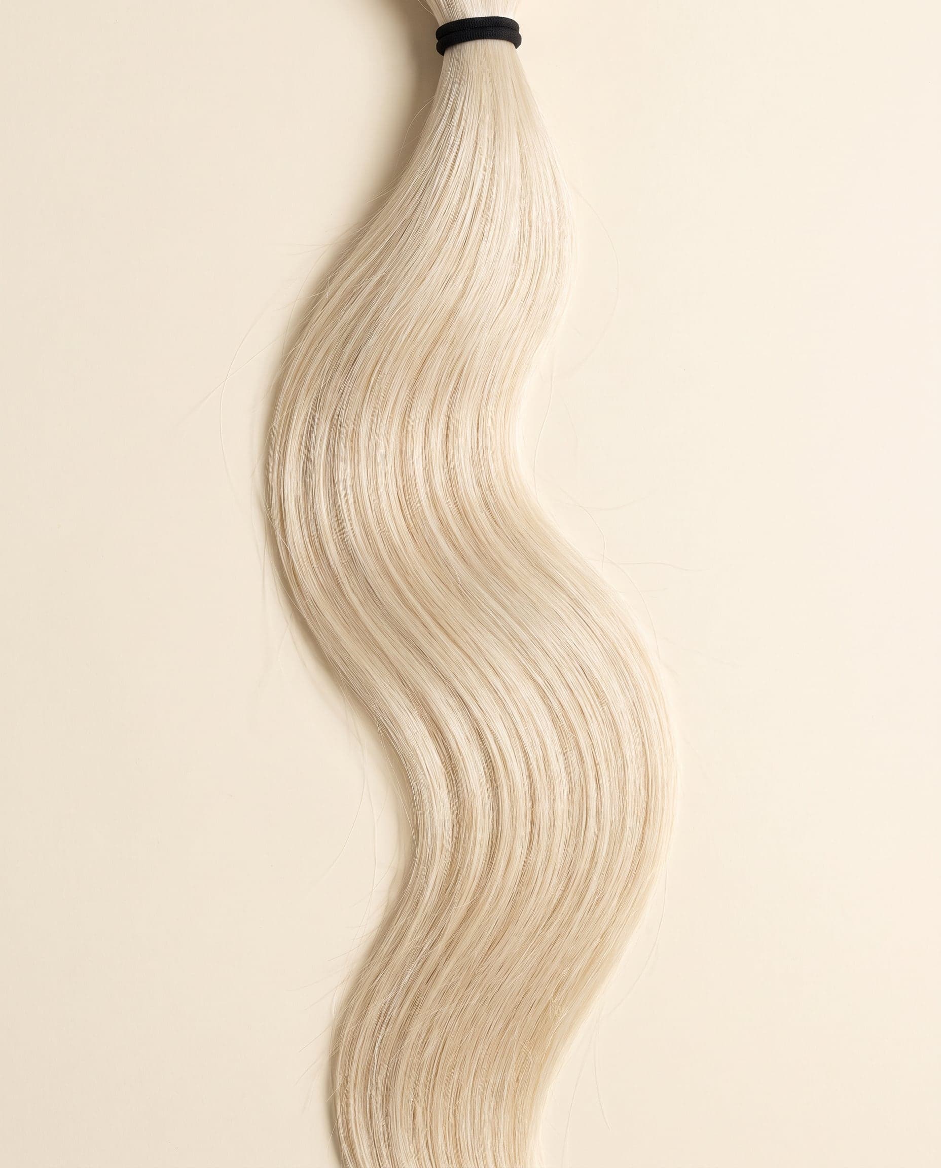 Human hair bundle in color 613 laid flat on a warm ivory background