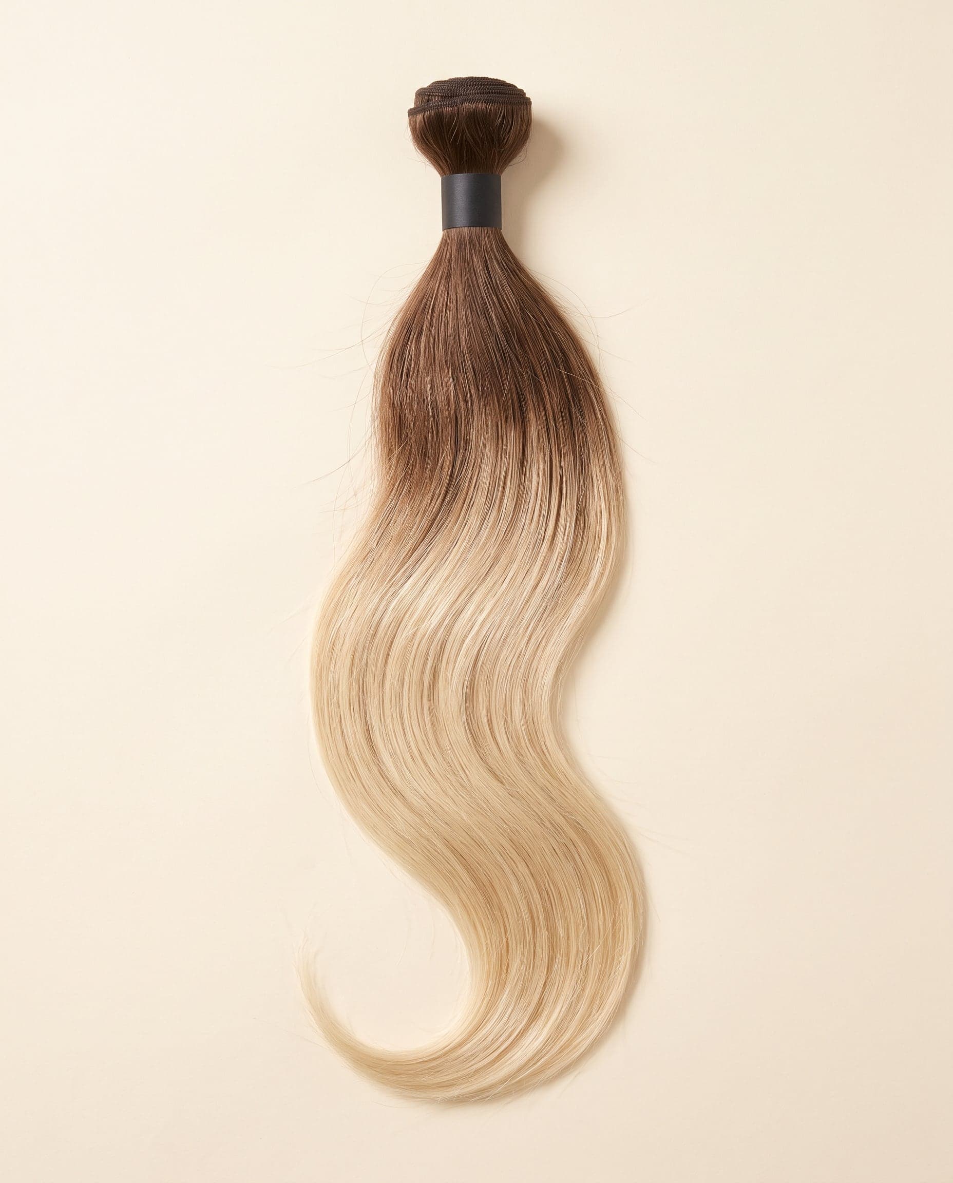 Human hair bundle in color A-4T/613 laid flat on a warm ivory background