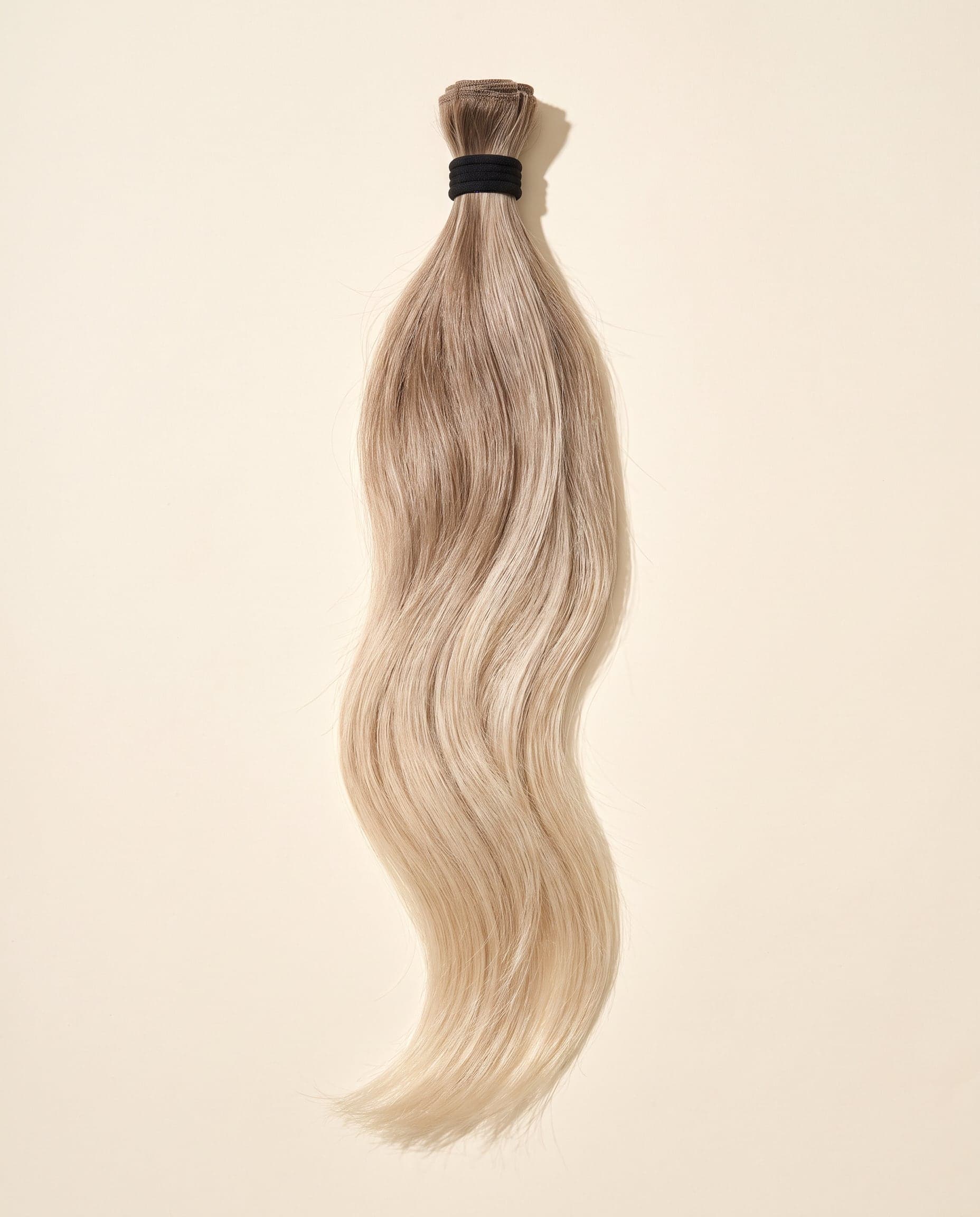 Human hair bundle in color A-8T/613 laid flat on a warm ivory background