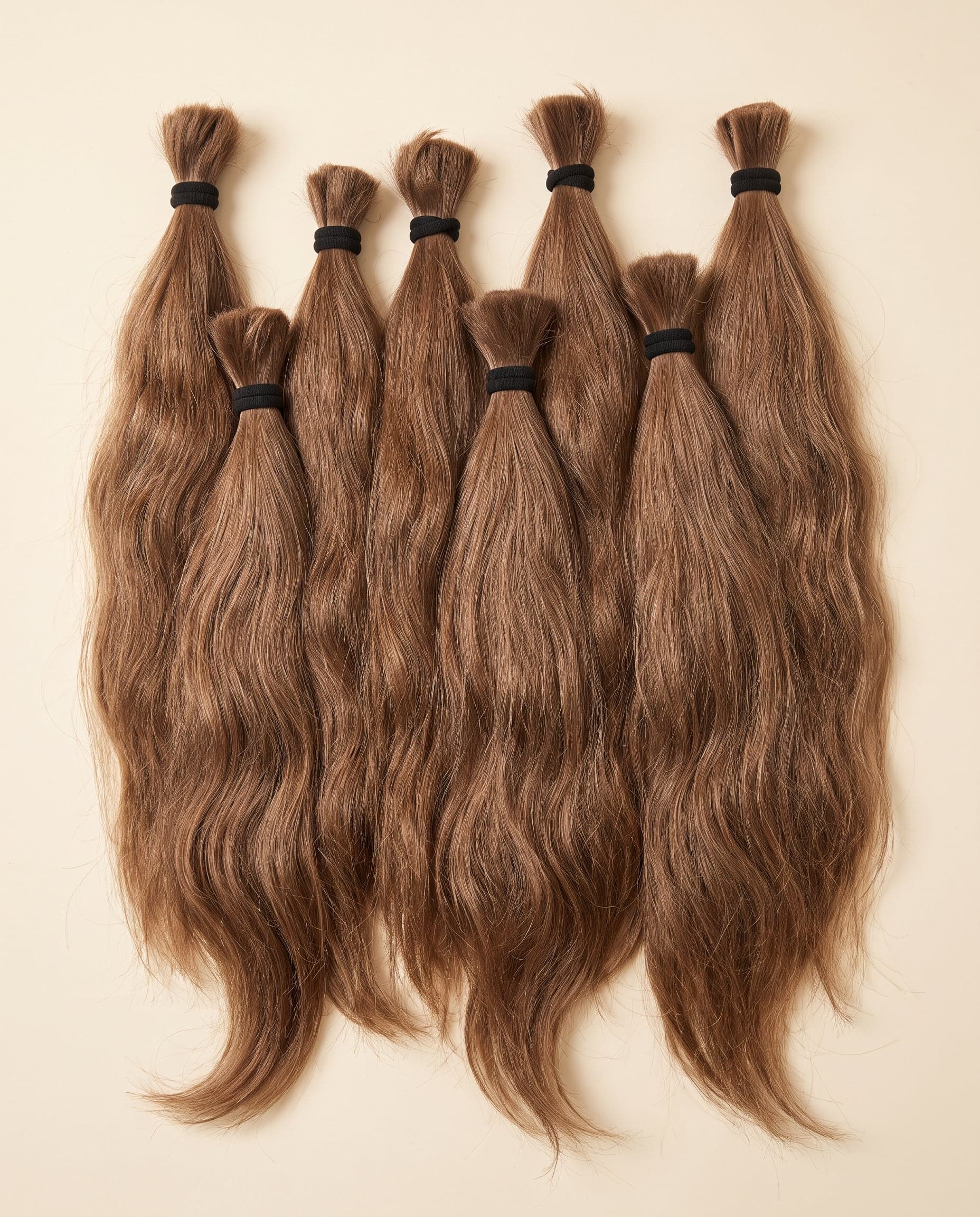Gold grade single-donor human hair bundles in natural light brown, wrapped in black and arranged in rows