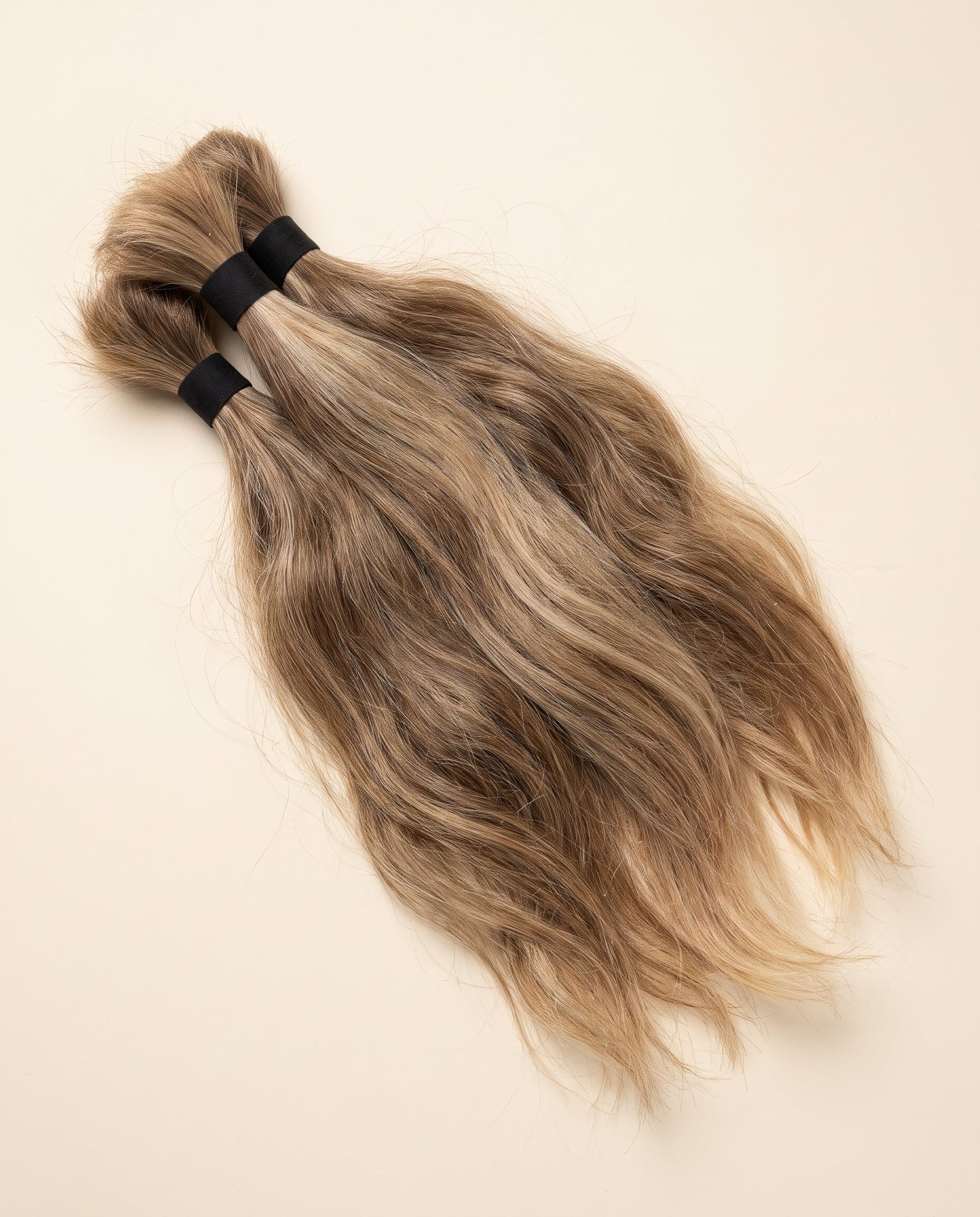 Three Premium grade bundles in honey blonde laid in an overlapping fanned arrangement on a warm ivory surface