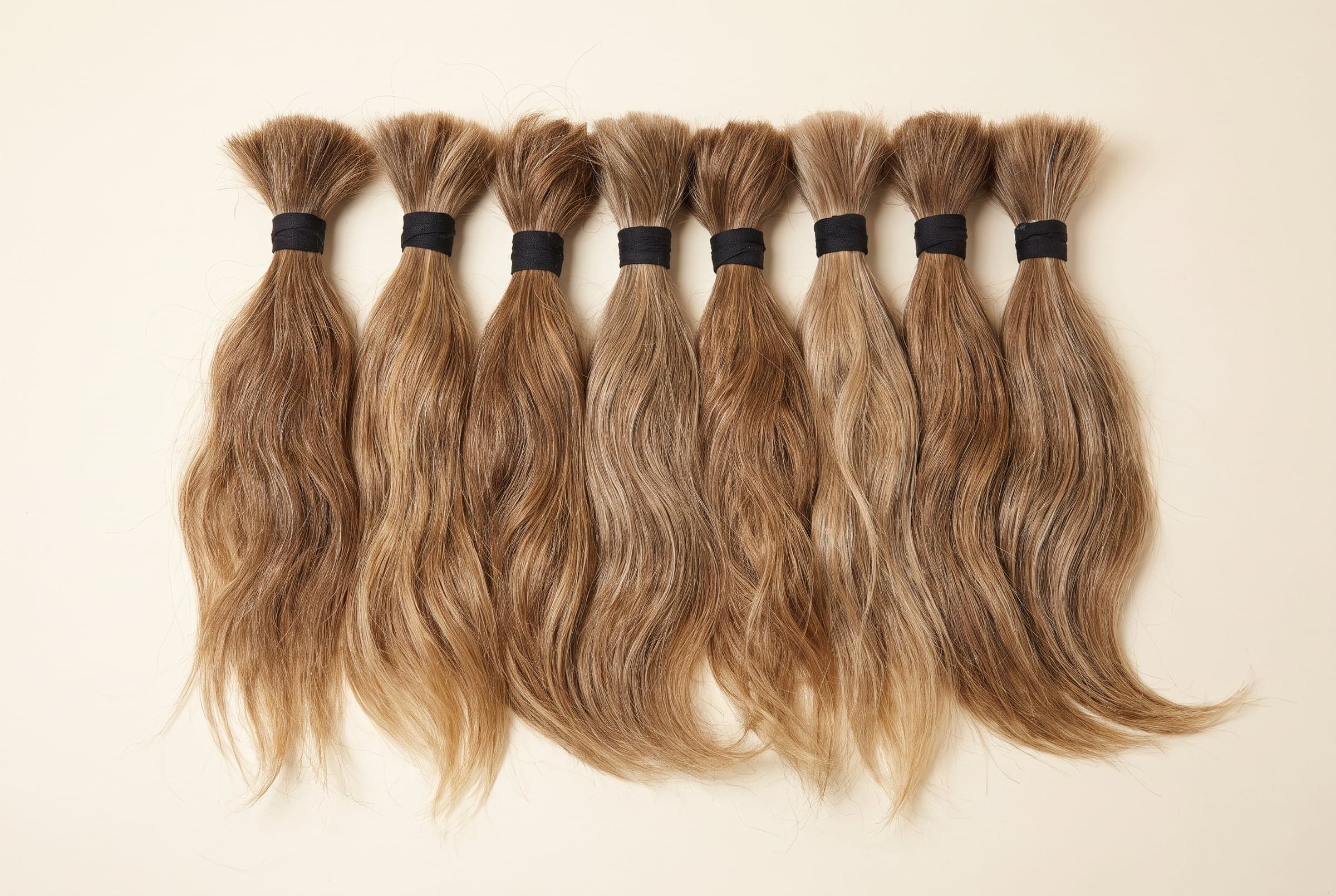 Premium grade hair bundles in natural blonde and light brown arranged in a row on an ivory surface