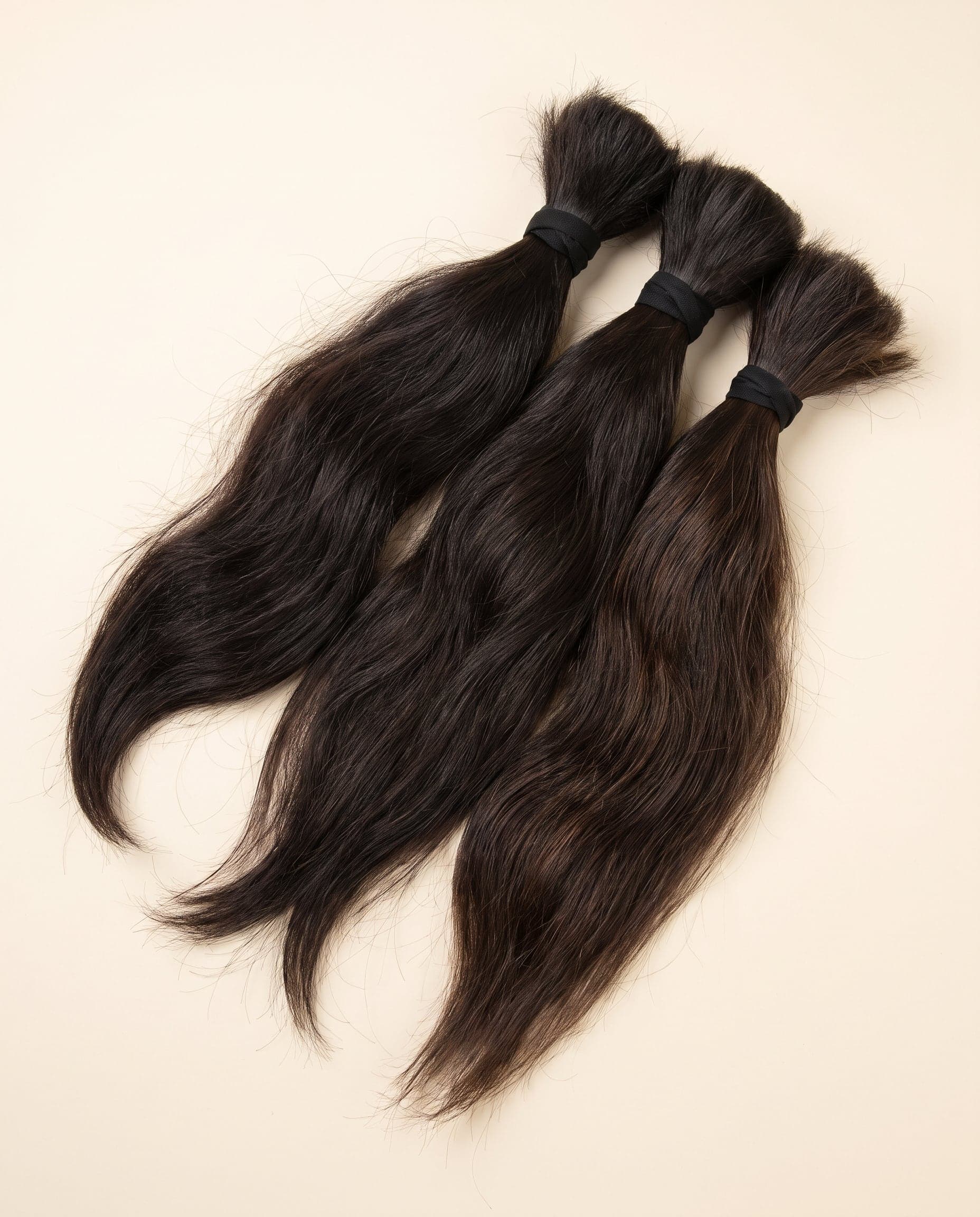 Three Silver grade bundles in dark natural brown laid in an overlapping fanned arrangement on a warm ivory surface